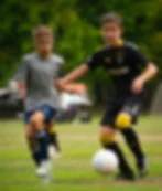 Two boys compete for a soccer ball on a grassy field, one in black Valor jersey and one in gray Everett shirt, focused and intense.