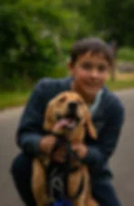 Boy hugs a panting golden retriever on a tree-lined road, both facing the camera.