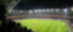 Nighttime soccer match in a packed stadium, with players on the bright green field and scoreboard showing 0–1.