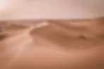 Lone person walking along wind-swept sand dunes in a vast desert at sunset