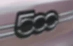 Close-up of a metallic car emblem on a mauve vehicle grille, showing chrome rings and stripes with a sleek, polished look