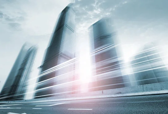 Blurred skyscrapers and light streaks over a city road under a cloudy sky, creating a fast, futuristic mood